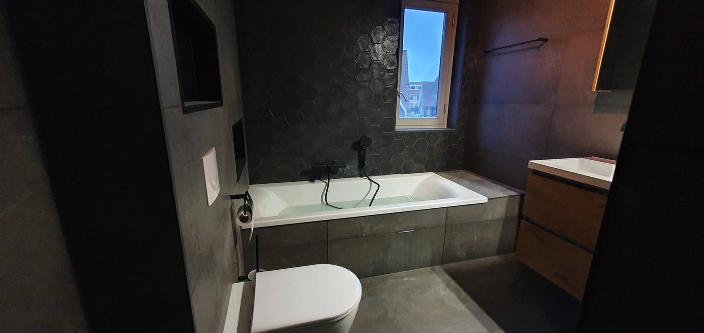 Badkamer met ingebouwd ligbad en donkere wandtegels