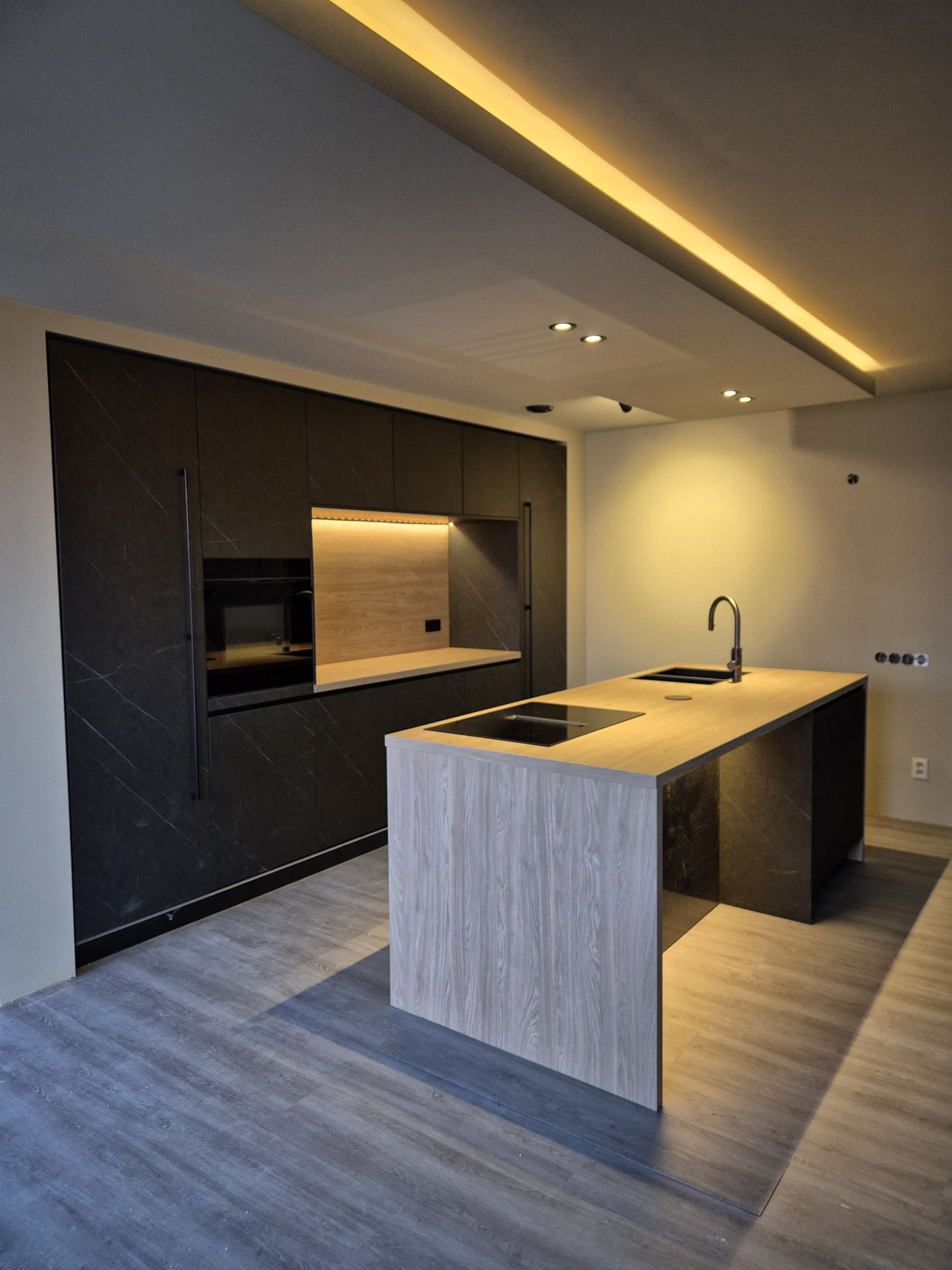 Kookeiland in lichte houtlook met zwarte kastenwand en LED-plafond