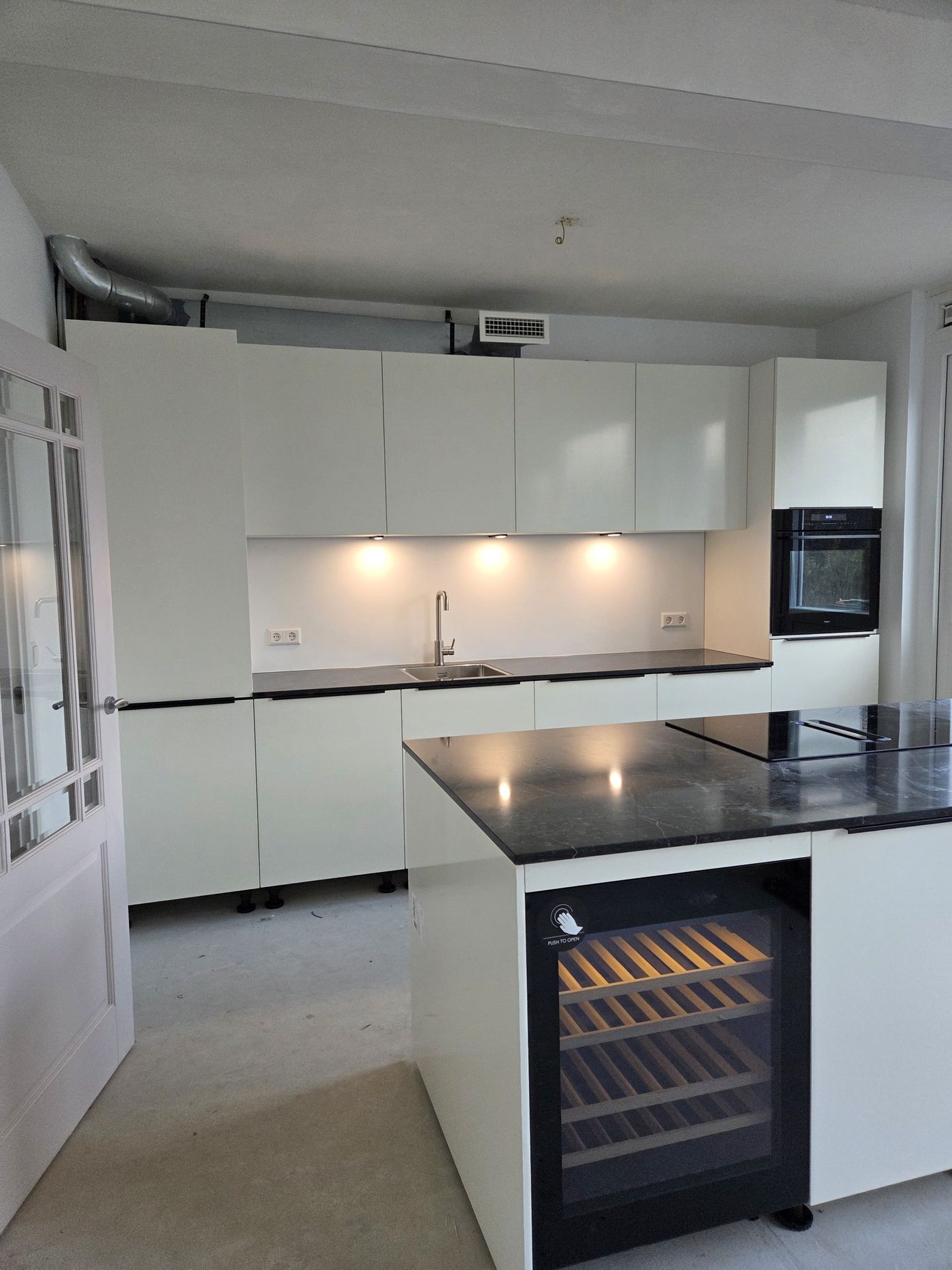 Witte keuken met kookeiland en ingebouwde wijnklimaatkast
