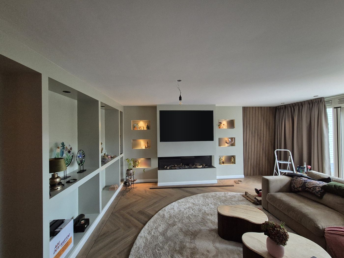Woonkamer met tv-wand, inbouwhaard, verlichte nissen en lamellenwand